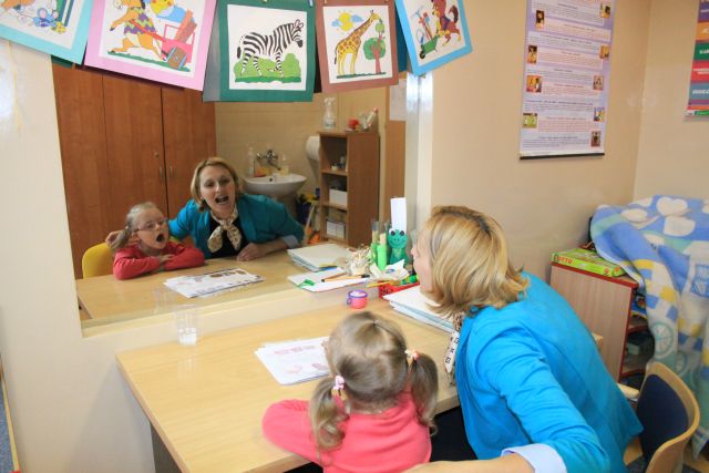 Zdjęcie przedstawia fragment terapii logopedycznej - terapeutę wraz z dzieckiem w trakcie wykonywania ćwiczeń logopedycznych